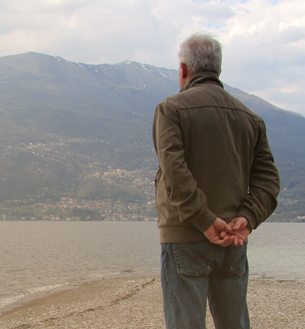 uomo anziano di spalle sulla spiaggia guarda il mare