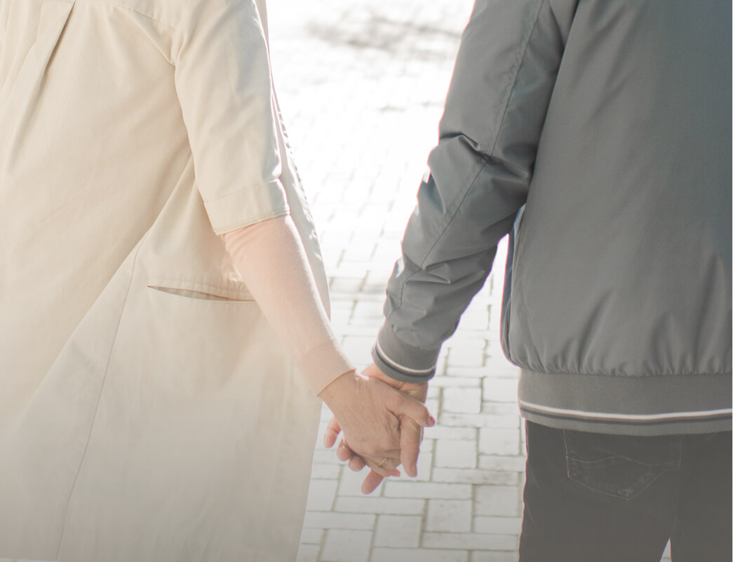Dettaglio di una coppia matura vista di spalle che si tiene per mano mentre cammina all'aperto, immagine che evoca compagnia e supporto reciproco