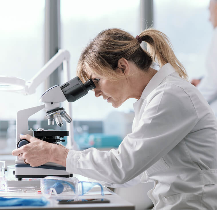 Ricercatrice scientifica in camice bianco al lavoro con un microscopio in laboratorio, simbolo dell'impegno costante nella ricerca e nel controllo qualità