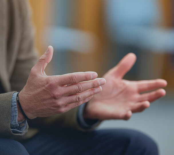 Dettaglio delle mani di un uomo che gesticola durante una conversazione, simbolo del dialogo aperto tra medico e paziente e dell'importanza della consulenza specialistica